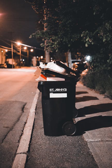 Three large black plastic rubbish bags, filled and loosely tied at the top, are placed on a paved sidewalk close to the curb. The bags appear to contain mixed waste, possibly including garden or domes