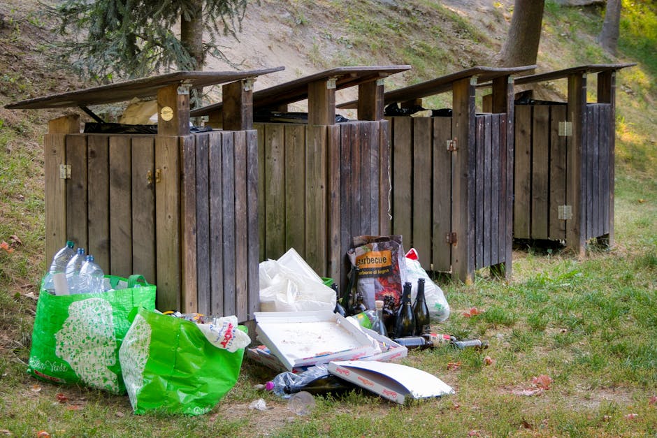 Close-up view of a pile of dark brown, glossy plastic rubbish bags stacked together, with some lightweight and semi-transparent white plastic sheets draped over and around them. The plastic bags show